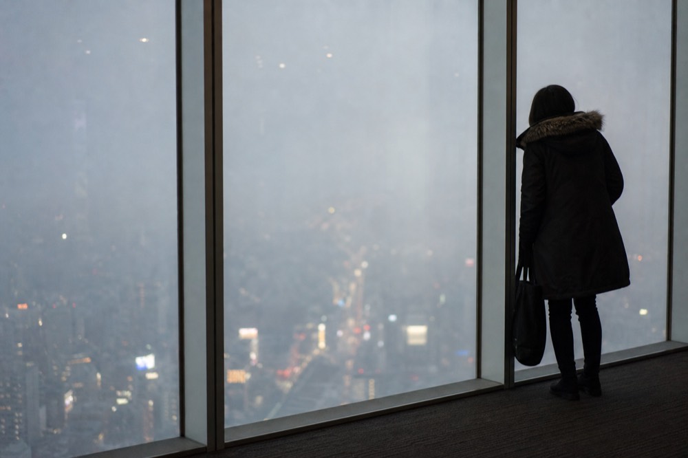 Low cloud pressing against the glass of a high indoor observation floor with the city dissolving into grey below