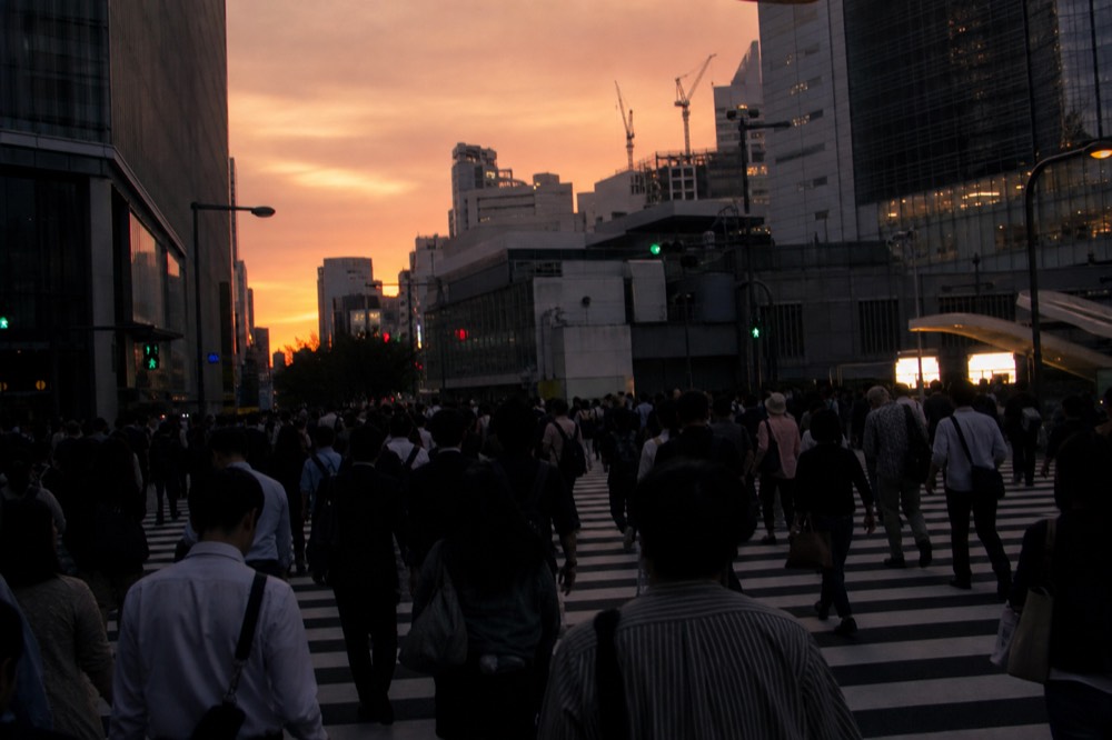 Dense crowd of pedestrians filling a wide painted intersection from all sides during a green signal in a Tokyo district