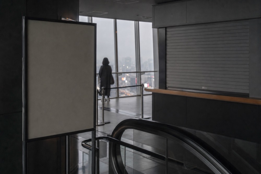 Sign board beside a closed walk up ticket window on floor fourteen of a Tokyo tower, escalator handrail in the foreground