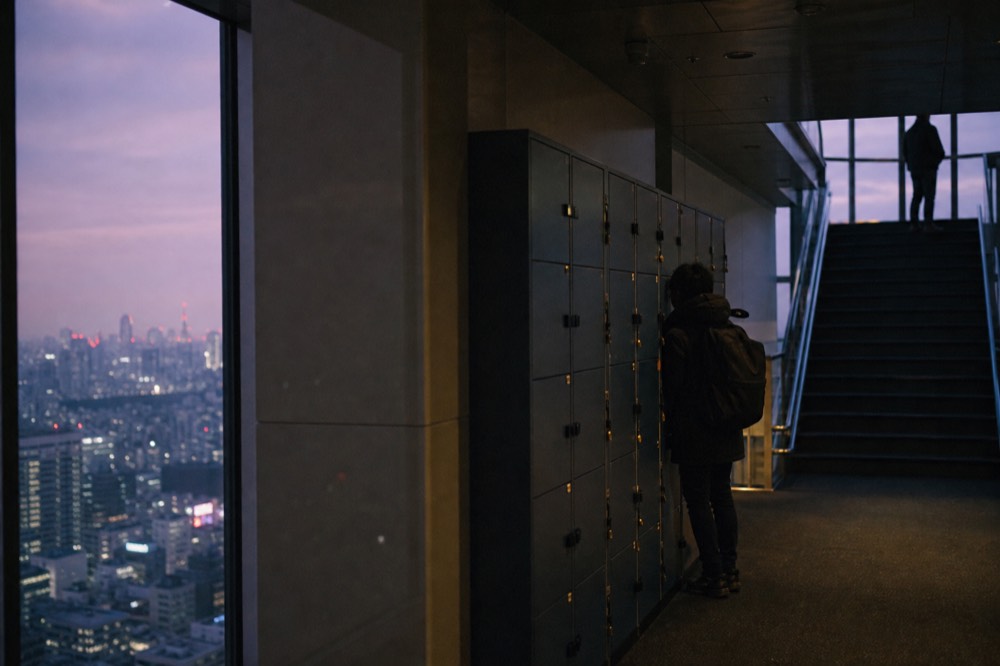 Row of small coin return lockers on an indoor observation floor with a visitor stowing a backpack before heading upstairs
