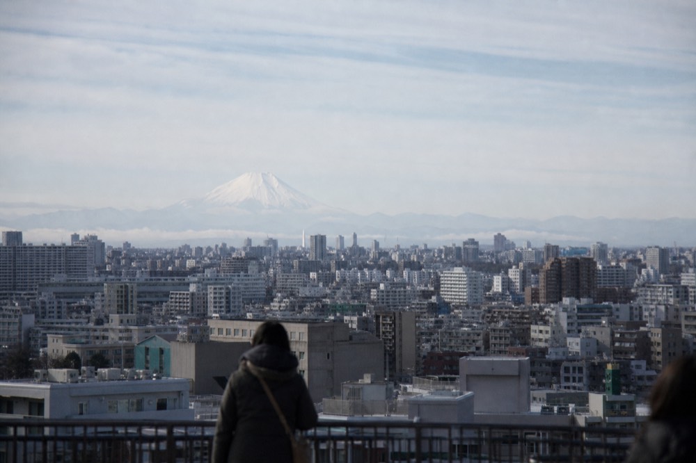 Distant snow-capped volcano visible above a haze layer beyond a sprawling city on a cold clear winter morning