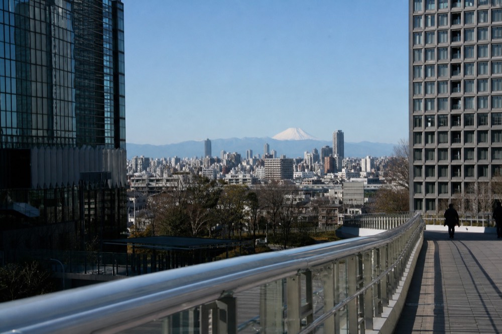 Winter city skyline under a pale blue sky with a distant white volcanic peak sharp on the western horizon