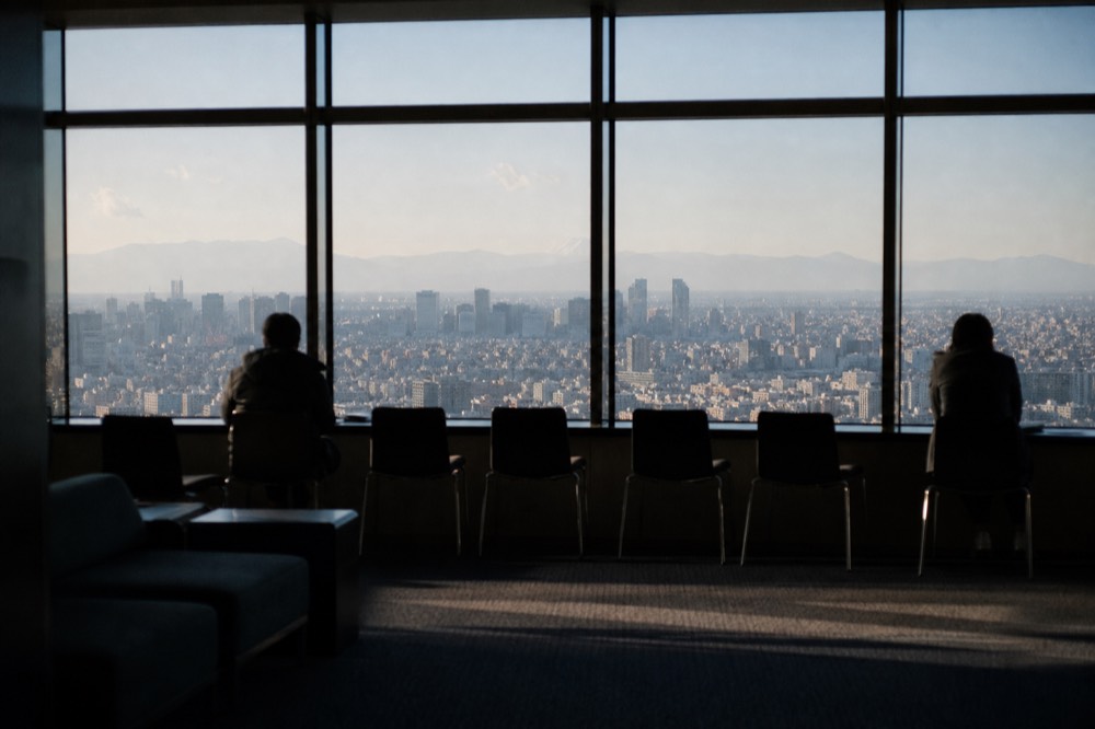 Interior observation lounge with wide glass windows looking west over Tokyo toward mountains on a clear winter afternoon