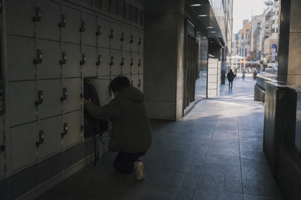 Bank of small coin-operated lockers in a dimly lit corridor with a visitor stowing a backpack into an open door