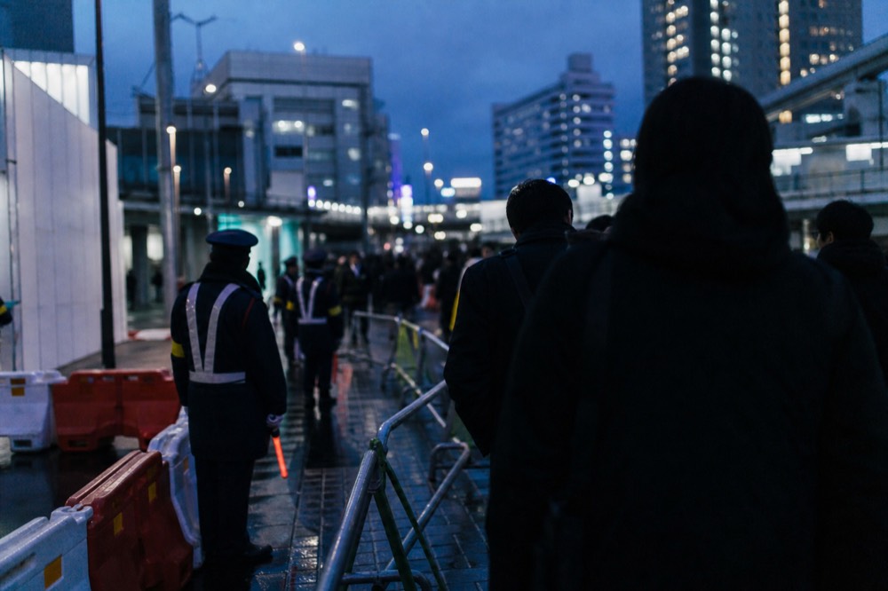 Evening street scene with crowd barriers and uniformed staff directing pedestrians past a busy station entrance