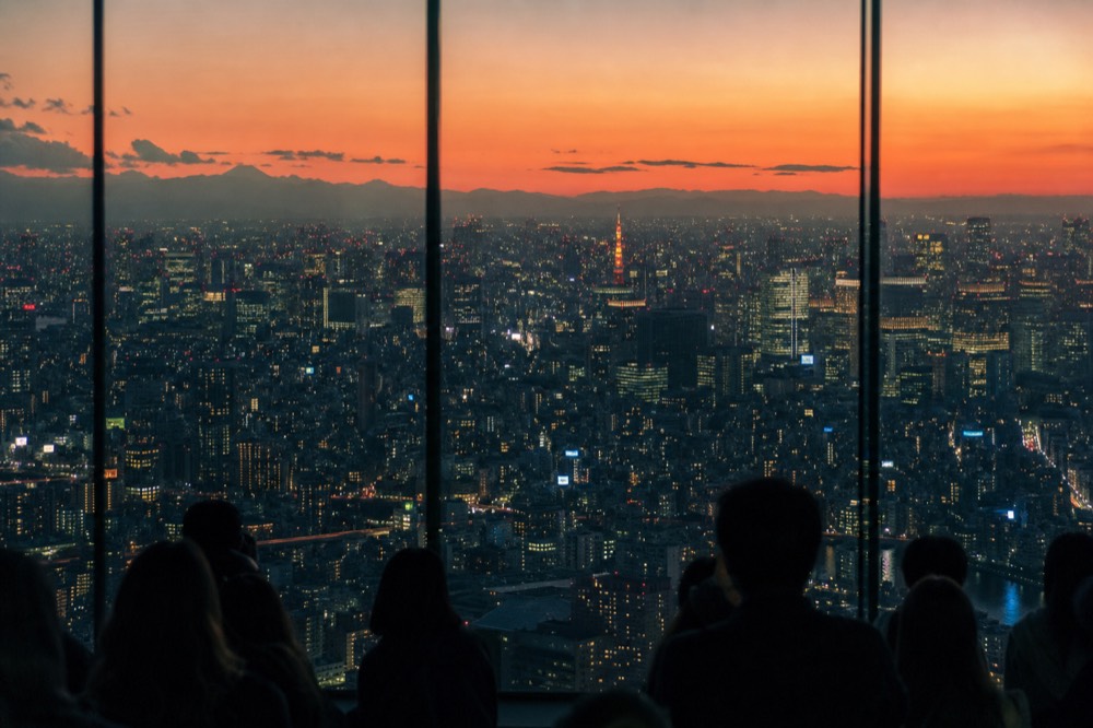 Wide evening view over central Tokyo from a high glass observation floor, illuminated towers receding into distant haze