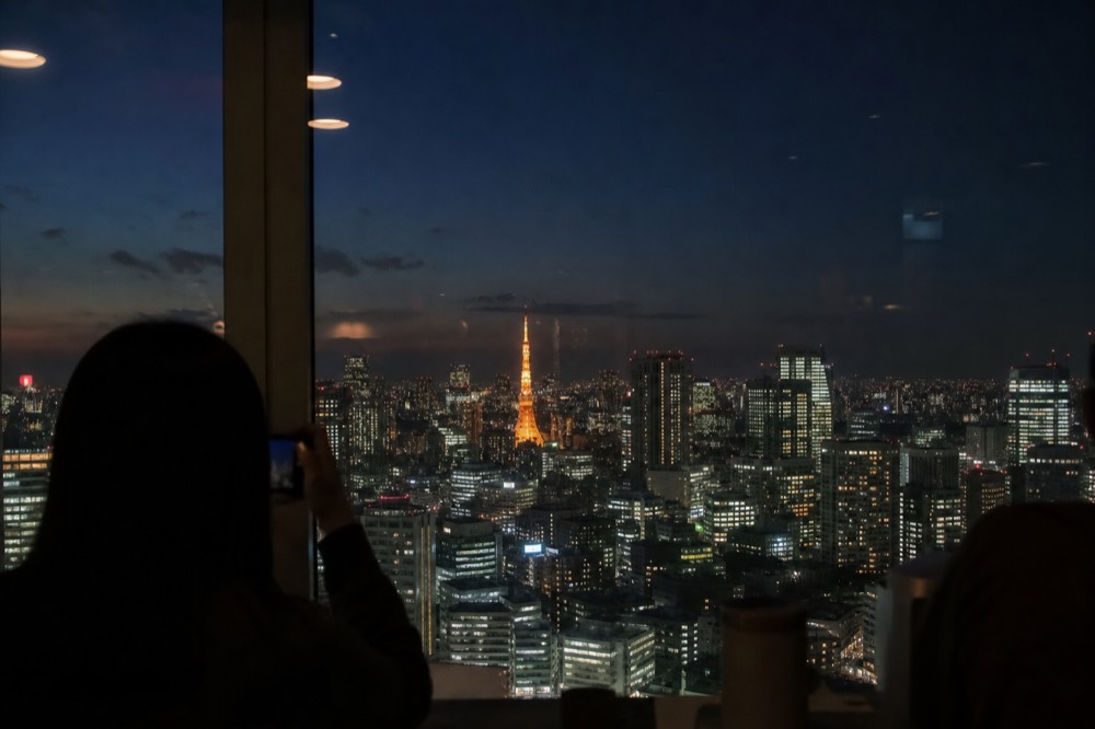 Orange-lit steel tower rising above a dark Tokyo skyline photographed from a distant high floor at night